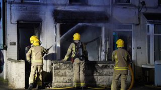 Emergency services work outside a house in Ballymena, Northern Ireland, as people protest over an alleged sexual assault in the Co Antrim town, Tuesday, June 10, 2025.