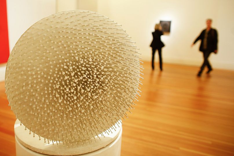 People walk behind the art work 'Weisse Muehle' ( White Mill), by artist Guenther Uecker during the press preview of the ZERO exhibition in Berlin, Friday, 20 March 2015. 