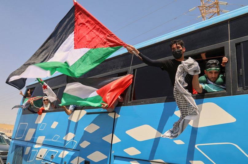 يلوح أعضاء قافلة إنسانية تضم ما لا يقل عن 1500 شخص، بالأعلام الفلسطينية من على متن حافلة أثناء توجه المجموعة إلى غزة، الثلاثاء 10 يونيو/حزيران 2025. 