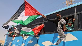 Members of a humanitarian convoy of at least 1,500 people wave Palestinian flags from a bus as the group travels toward Gaza in Zawiya, 10 June, 2025