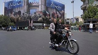 مردی در حالی که با موتورسیکلت خود سوار می شد، یک تابلوی پیروزی را به روی پرچم ضد اسرائیلی نشان می دهد که سربازان ایرانی در حال حمله به خاک اسرائیل هستند، در میدان انقلاب اسلامی