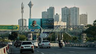 Vehicles drive on a highway with residential towers and the Milad telecommunications tower visible in the background in northern Tehran, Iran, Friday, June 13, 2025. 