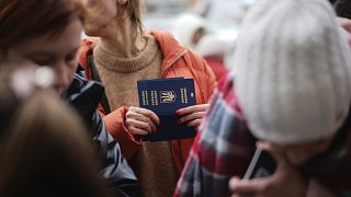 A woman holds Ukrainian passports as she waits to register for a bus which will take refugees to Germany, at the train station in Przemysl, Poland, Thursday, March 3, 2022. 