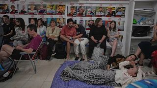 People take shelter next to photographs of Israeli hostages abducted during the Hamas attack, during air raid sirens warning of incoming strikes by Iran, 19 June 2025.