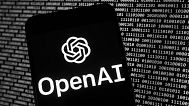 The OpenAI logo appears on a mobile phone in front of a computer screen with random binary data, Thursday, March 9, 2023, in Boston