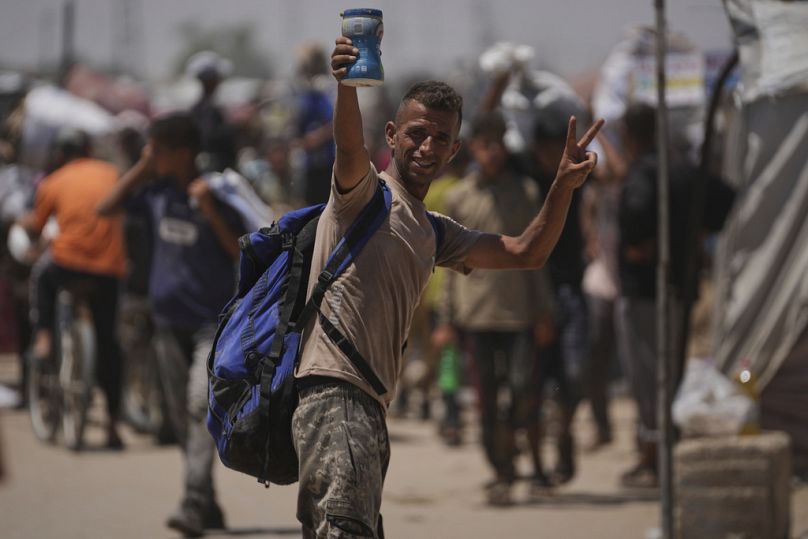 رجل فلسطيني يلوّح بعلامة النصر ويحمل علبة طحينة، في رفح جنوب قطاع غزة، 26 حزيران/يونيو 2025.