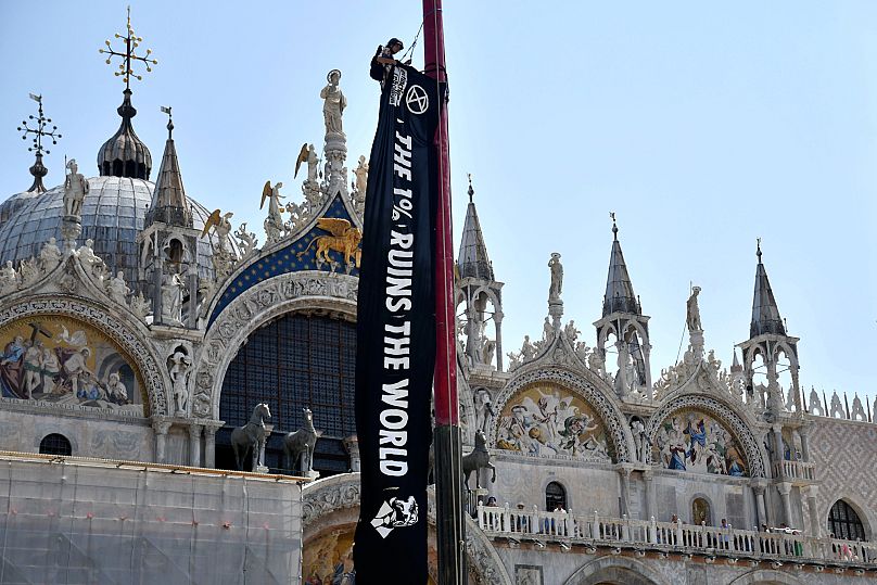 An activist from Extinction Rebellion unfolds a banner in front of St. Mark's Basilica in Venice