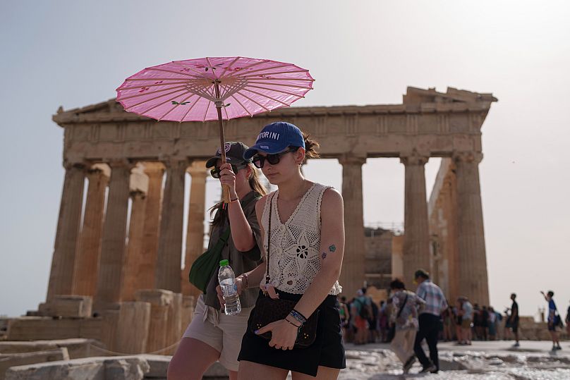 Turistë me çadër shëtisin përpara Partenonit në Akropolin e lashtë në qendër të Athinës, 12 qershor 2024