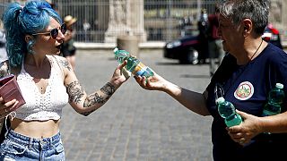 A civil protection volunteer distributes free bottles of water to tourists next to the Colosseum in Rome, Thursday, Aug. 12, 2021