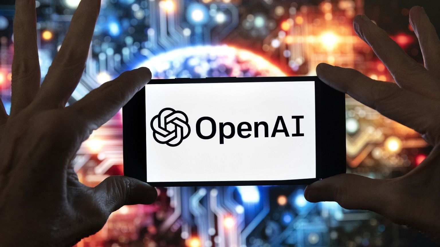 The OpenAI logo is displayed on a cell phone in front of an image generated by ChatGPT.