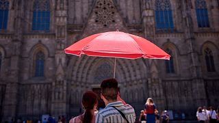 A couple protect themselves from the sun with an umbrella while looking at Barcelona's cathedral.
