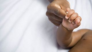 A baby holds a woman's finger.