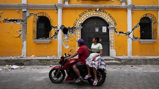 A couple ride past a community hall damaged as a result of dozens of earthquakes and aftershocks recorded in a matter of hours, Santa Maria de Jesus, Guatemala, July 9, 2025. 