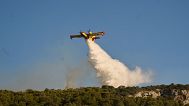 A firefighting airplane drops water as a wildfire burns in Rafina, east of Athens, Greece, Thursday, July 3, 2025, with several houses destroyed from the fire in the area.