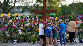 Dan Beazley, left, holds a large cross as he prays with visitors at a memorial for flood victims on Thursday, July 10, 2025, in Kerrville, Texas