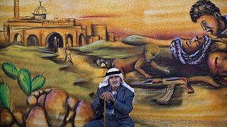  یک پناهنده فلسطینی در روز چهارشنبه ۱۸ ژوئن ۲۰۱۴ با دیواری تزئین شده با نقاشی دیواری که درگیری اسرائیل و فلسطینی را نشان می دهد 