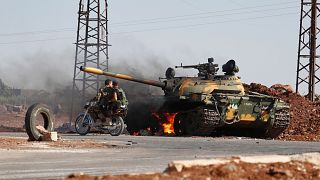 Syrian government soldiers on a motorcycle pass by a burning tank on the outskirts of Sweida city, 14 July, 2025