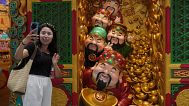 A woman takes a selfie with gods of fortune displayed outside a store selling prosperity items at a shopping mall, in Beijing. 14 July 2025.