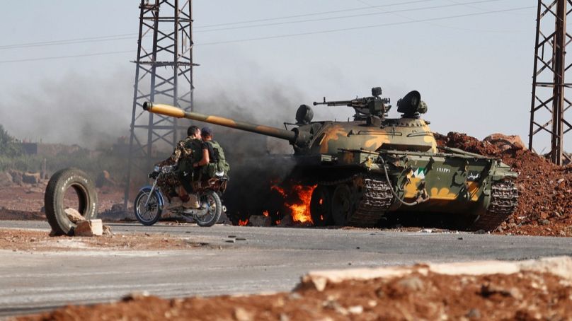 Soldados del Gobierno sirio en una motocicleta pasan junto a un tanque en llamas en las afueras de la ciudad de Al Sueida, en el sur de Siria, el lunes 14 de julio de 2025.