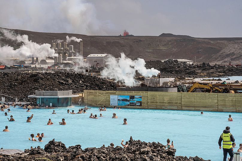 Le lagon bleu avec des gens qui se baignent alors que le cratère volcanique crache de la lave en arrière-plan à Grindavik, en Islande, le 2 juin 2024.