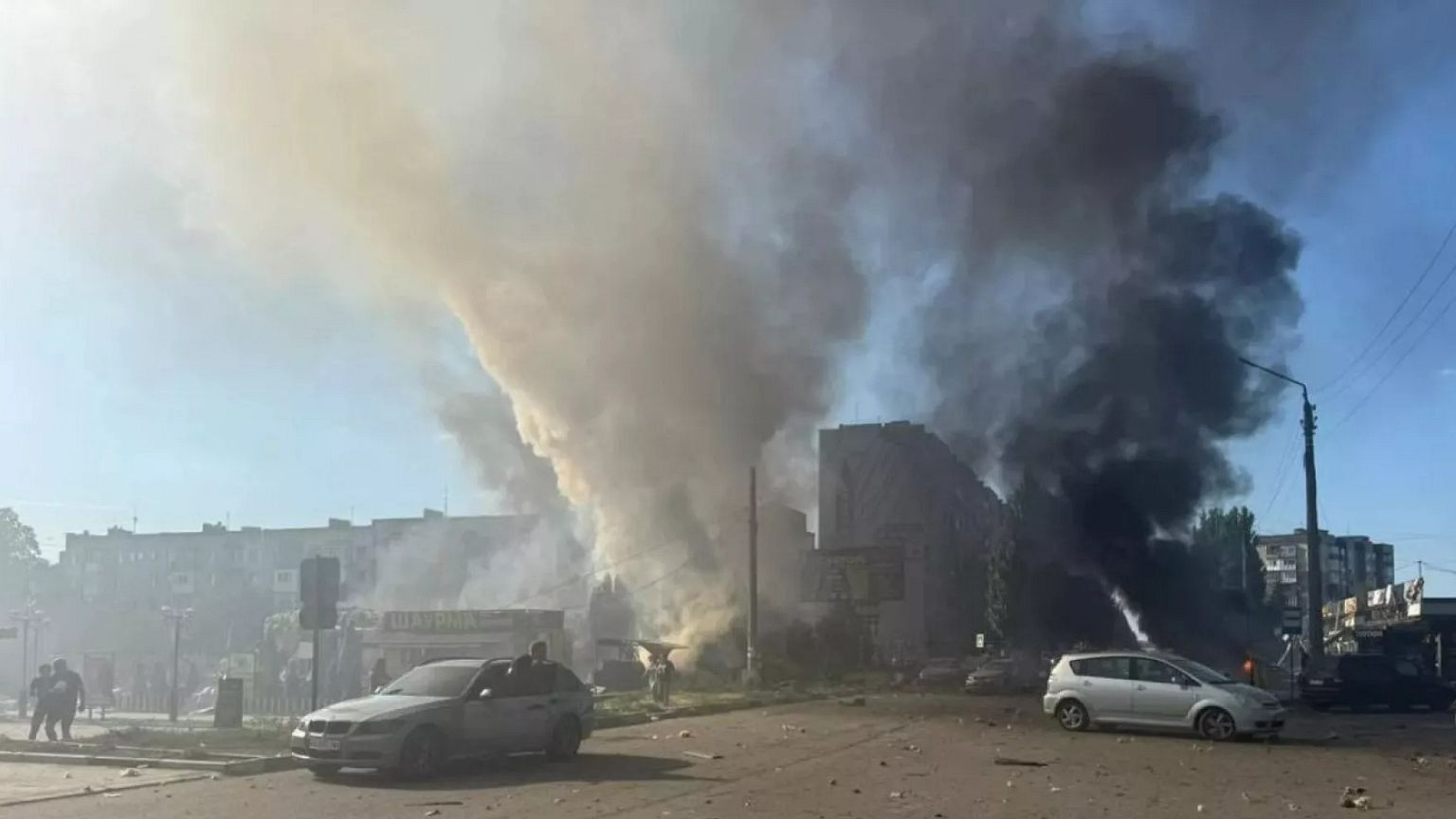Dos columnas de humo salen de vehículos y escaparates en llamas en el centro de Dobropillia tras un ataque aéreo ruso de 500 kg el 16 de julio de 2025.