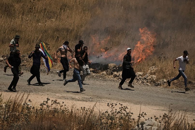 Syrian Druze run away from tear gas fired by Israeli soldiers as they protest on the Syrian side of the border with Israel, 16 July, 2025