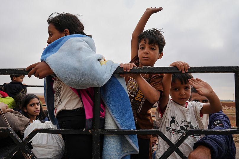 Familias beduinas sirias viajan en la parte trasera de camiones que transportan sus pertenencias en un convoy liderado por vehículos de la Media Luna Roja en Busra al-Harir.