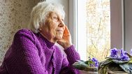 An older woman looks out the window.