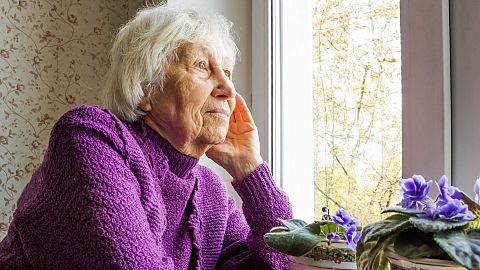 An older woman looks out the window.