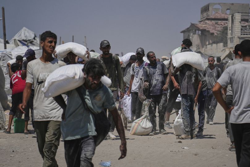 فلسطينيون ينقلون أكياس طحين من قافلة مساعدات إنسانية وصلت إلى مدينة غزة من شمال القطاع، الأحد 27 يوليو 2025.