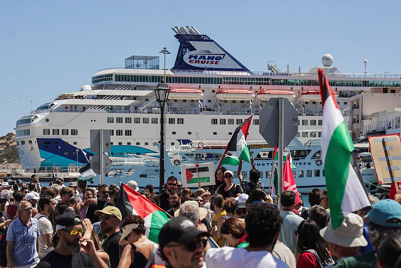 Manifestantes propalestinos se reúnen durante la llegada de un barco que transporta turistas israelíes, al fondo, en el puerto de Agios Nikolaos, en la isla de Creta, Grecia.