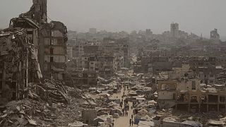 People walk along a street lined with destroyed buildings following Israeli bombardments during the Israel-Hamas war in the Gaza Strip, 29 July, 2025