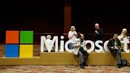 Attendees of Microsoft Corp.'s annual shareholders meeting sit on a Microsoft sign while waiting for the meeting to begin. December 2014.