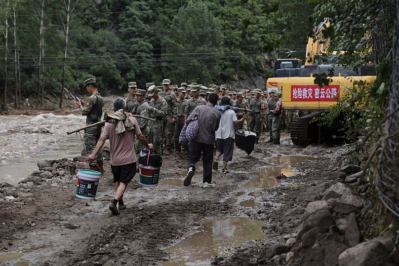 Miyun bölgesinde şiddetli yağışlar sonucu selden zarar gören yolda mahsur kalan köylüleri kurtarmak için yola çıkan askerlerin yanından geçen köylüler, 29 Temmuz 2025.