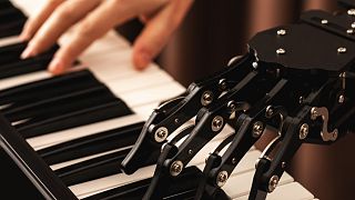 A human and robot play piano.