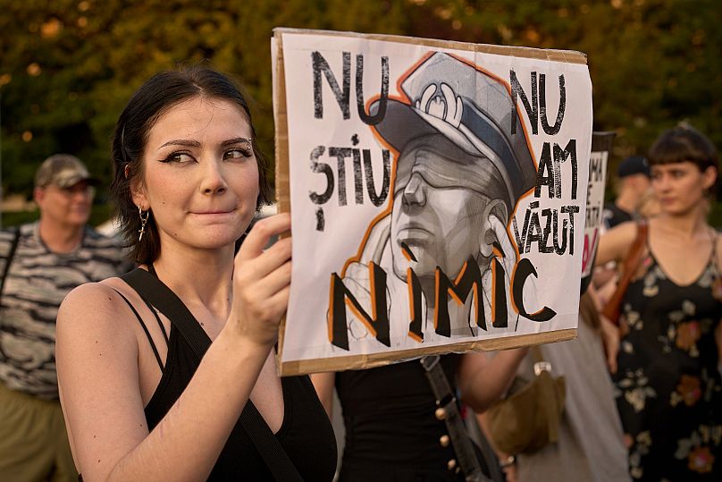 A woman grimaces holding a banner that reads "I don't know - I haven't seen anything" during a protest outside the government headquarters in Bucharest, Romania, Wednesday, Ju