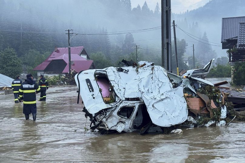 In this image released by the Romanian Emergency Services Suceava (ISU Suceava) first responders walk by damaged vehicles after a flash flood in the village of Brosteni, north