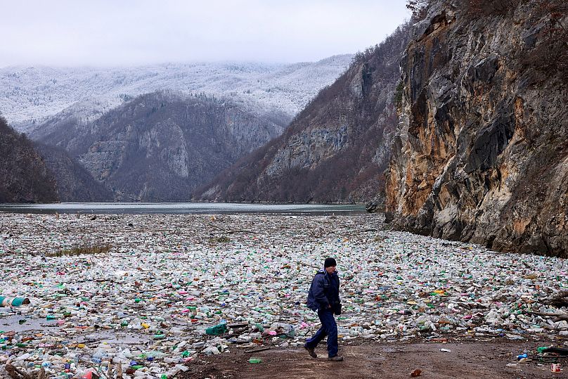 A man walks past waste floating in the Drina River near Visegrad, Bosnia,.