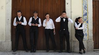 O empregado de mesa João Sintra, segundo à direita, ajeita a gravata enquanto a empregada Maria Almas, ao centro, fuma um cigarro durante uma pausa com os colegas de trabalho no centro de Lisboa. 27 de abril de 2013.