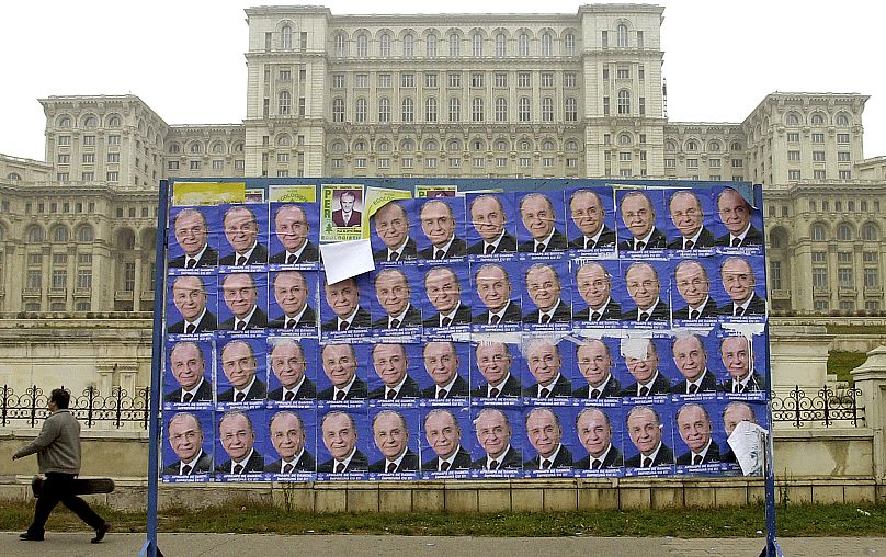 FILE: A man passes by posters of former Romanian President Ion Iliescu, backdropped by the Palace of Parliament in Bucharest, 25 November 2000