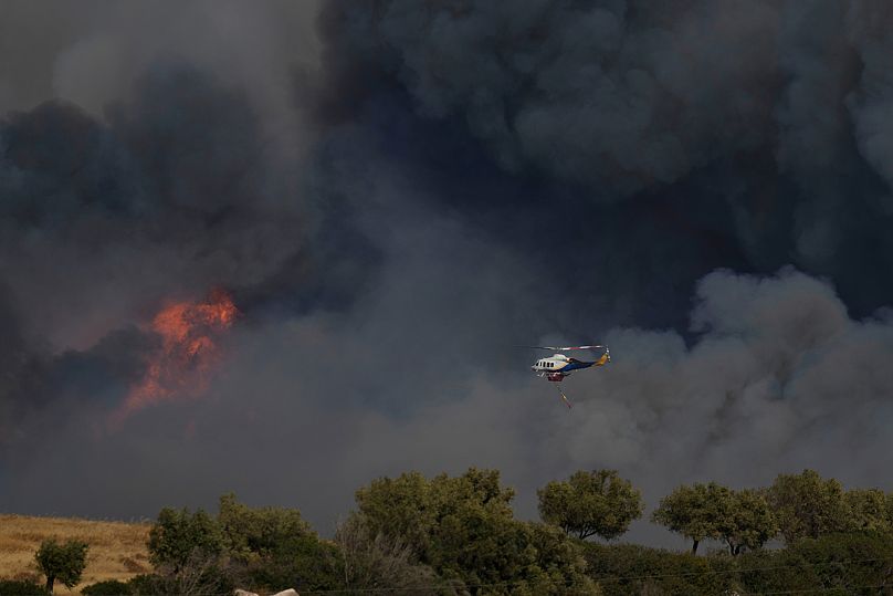 A helicopter flies through smoke from a fire at Keratea, outskirt of Athens, on Friday, Aug. 8, 2025.