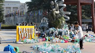 Benjamin Von Wong, right, a Canadian artist and activist, heaps piles of plastic waste onto a large sculpture that he designed in front of the United Nations office in Geneva.