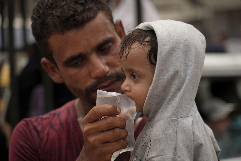  يعطي رجل لطفل الماء من كيس بلاستيكي اشتراه للتو ، في مدينة غزة، الثلاثاء 12 أغسطس/آب 2025.
