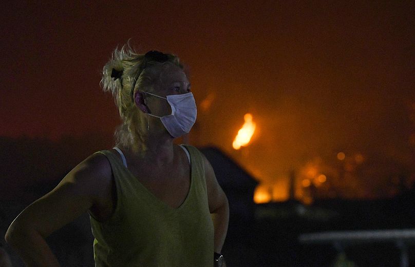Un habitant portant un masque observe les flammes se rapprocher du village de Kaminia, près de la ville de Patras, dans l'ouest de la Grèce, mardi 12 août 2025.