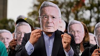 Varios partidarios del expresidente colombiano Álvaro Uribe muestran caretas de su rostro ante el tribunal donde fue declarado culpable de manipulación de testigos y soborno.