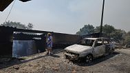 Una mujer pasa junto a un coche y una casa calcinados tras un incendio forestal en Caridade, al noroeste de España, el jueves 14 de agosto de 2025.