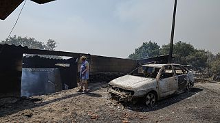 Una mujer pasa junto a un coche y una casa calcinados tras un incendio forestal en Caridade, al noroeste de España, el jueves 14 de agosto de 2025.