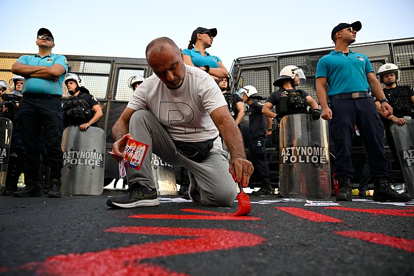 A protester paints a slogan on the ground during a rally to protest the arrival of a cruise ship with Israelis in Piraeus, 14 August, 2025