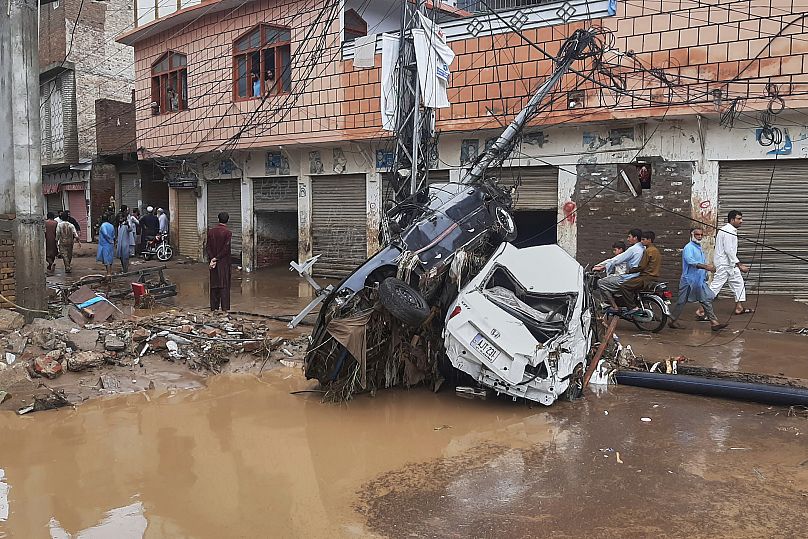 Residents walk next to damaged cars stuck to an electric pole following flash flooding in a neighbourhood of Mingora, 15 August, 2025