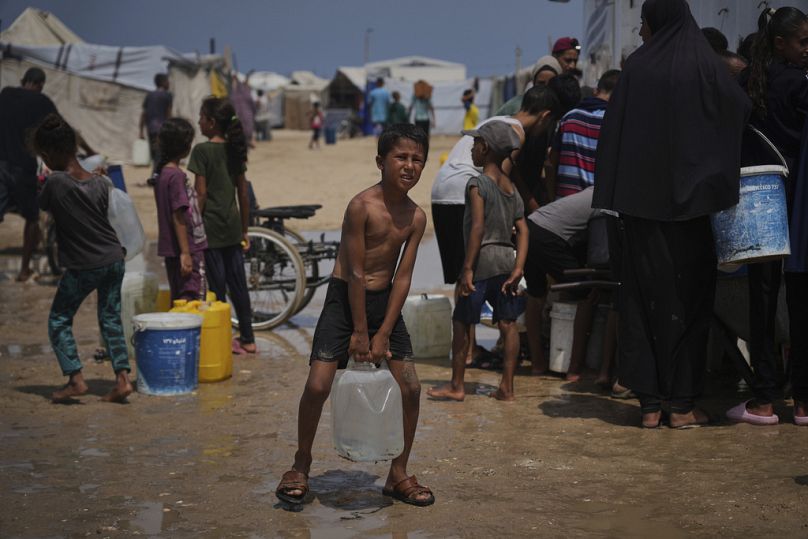 نازحون فلسطينيون يتجمعون لجمع مياه من شاحنة خلال موجة حر في مخيم عشوائي بخان يونس، 13 أغسطس 2025.